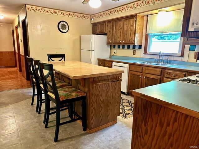 kitchen with ceiling fan, sink, a kitchen breakfast bar, white appliances, and a kitchen island