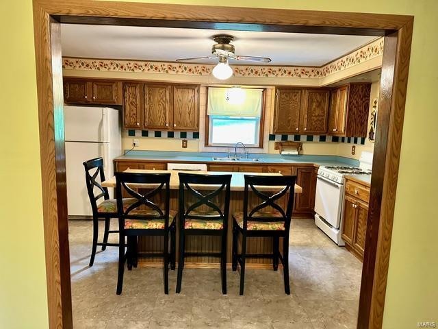 kitchen with a kitchen breakfast bar, ceiling fan, sink, and white appliances