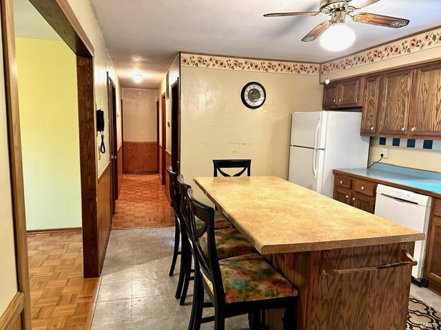 kitchen featuring ceiling fan, light parquet floors, white appliances, a breakfast bar, and a kitchen island