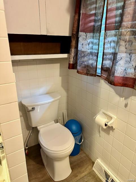 bathroom featuring wood-type flooring, toilet, and tile walls