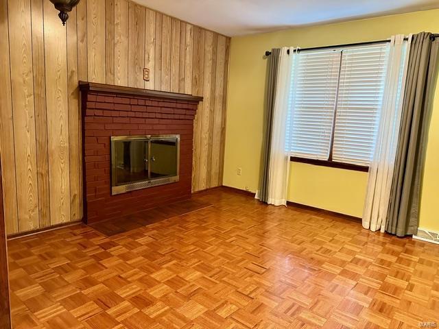 unfurnished living room with light parquet flooring, a brick fireplace, and wooden walls