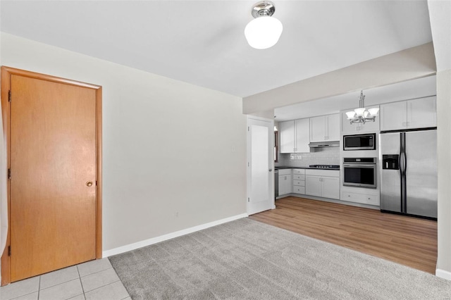 kitchen featuring pendant lighting, stainless steel appliances, dark countertops, white cabinetry, and under cabinet range hood