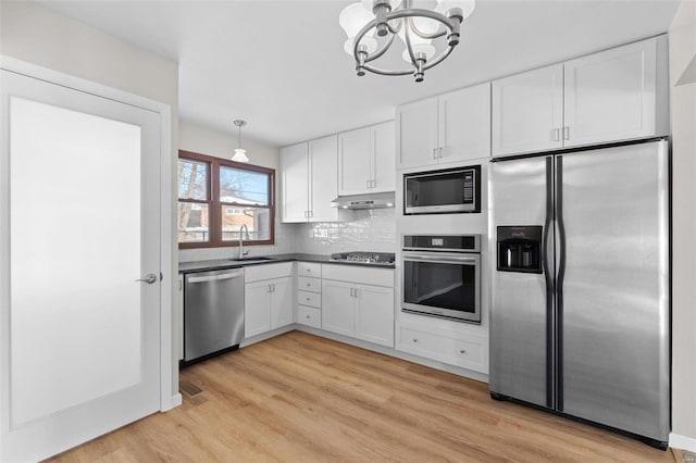 kitchen with pendant lighting, stainless steel appliances, dark countertops, white cabinets, and under cabinet range hood