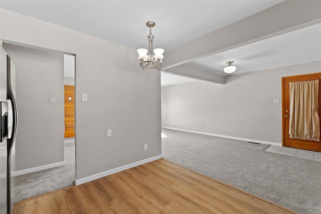 unfurnished room featuring an inviting chandelier, baseboards, light wood finished floors, and beam ceiling