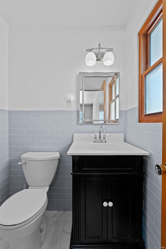 half bathroom featuring a wainscoted wall, vanity, toilet, and tile walls