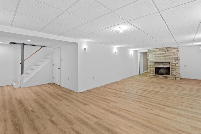 finished basement featuring light wood-type flooring, stairway, a drop ceiling, and a stone fireplace