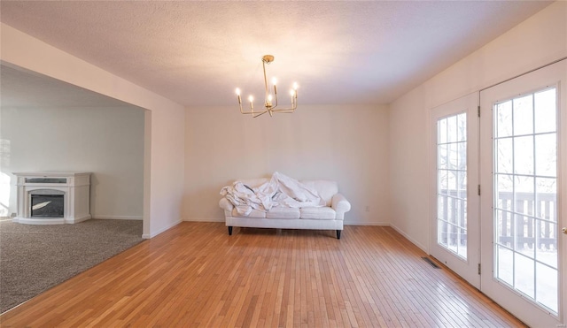 unfurnished room with an inviting chandelier, light hardwood / wood-style flooring, and a textured ceiling