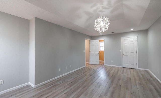 unfurnished room featuring light hardwood / wood-style floors, a chandelier, and a tray ceiling