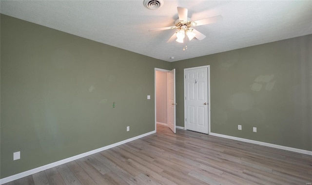 empty room with ceiling fan, light wood-type flooring, and a textured ceiling