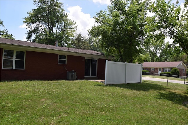 rear view of house with central air condition unit and a yard