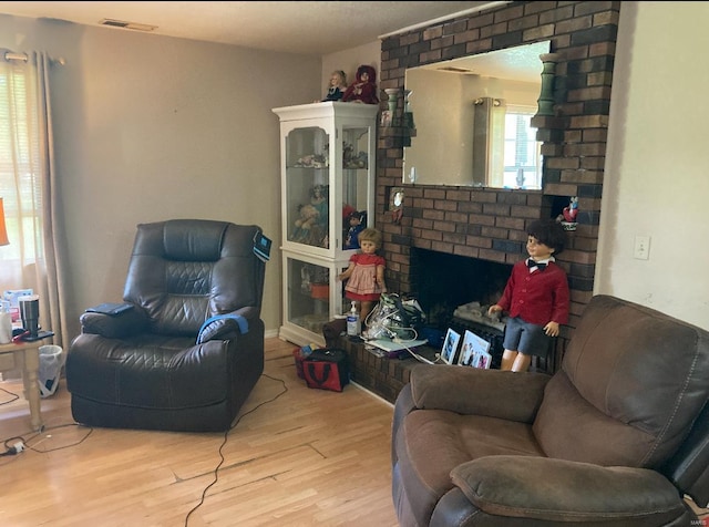 living room with light hardwood / wood-style floors, brick wall, and a brick fireplace