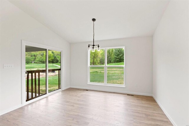 empty room with a healthy amount of sunlight, light hardwood / wood-style flooring, lofted ceiling, and a notable chandelier