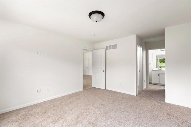 unfurnished bedroom featuring ensuite bathroom, light colored carpet, and sink