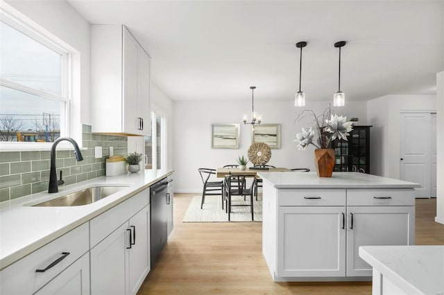 kitchen with light wood-type flooring, stainless steel dishwasher, sink, decorative light fixtures, and white cabinetry