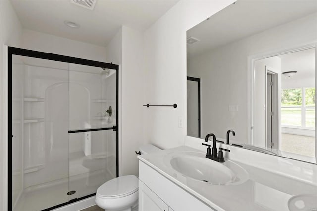 bathroom featuring a shower with door, vanity, and toilet