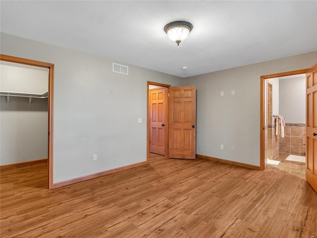 unfurnished bedroom featuring light hardwood / wood-style floors, ensuite bathroom, a closet, and a walk in closet