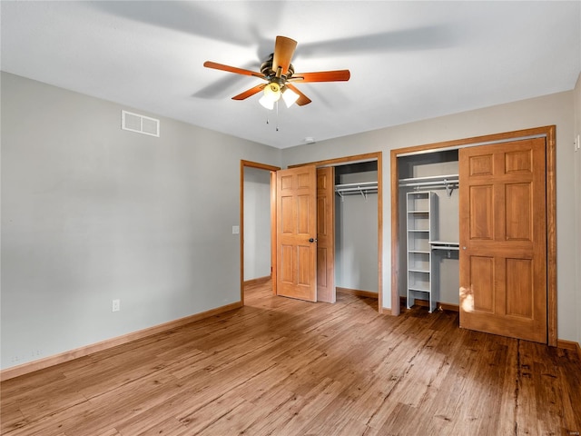 unfurnished bedroom featuring ceiling fan, hardwood / wood-style flooring, and multiple closets