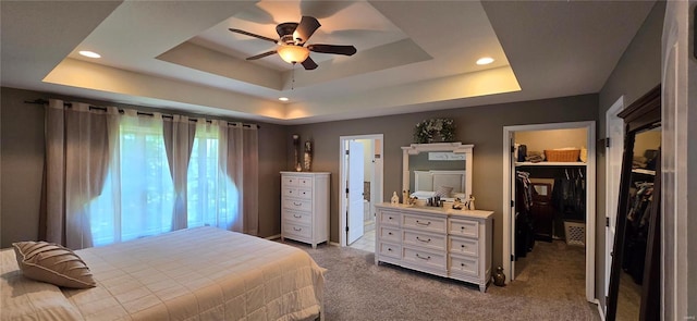 carpeted bedroom with a closet, ceiling fan, a raised ceiling, and a walk in closet