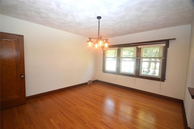 spare room featuring wood-type flooring, a textured ceiling, and a notable chandelier