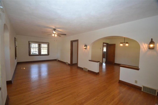 empty room featuring ceiling fan with notable chandelier and dark hardwood / wood-style floors