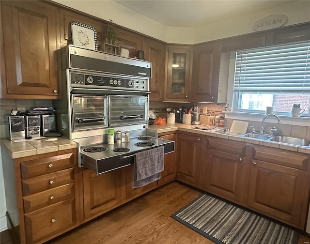 kitchen featuring stainless steel stovetop, sink, black oven, tile counters, and wood-type flooring