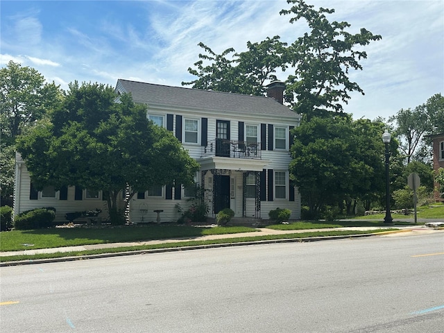 colonial home with a balcony and a front lawn