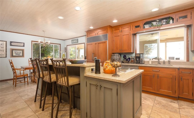 kitchen with paneled refrigerator, a kitchen island with sink, sink, a chandelier, and hanging light fixtures