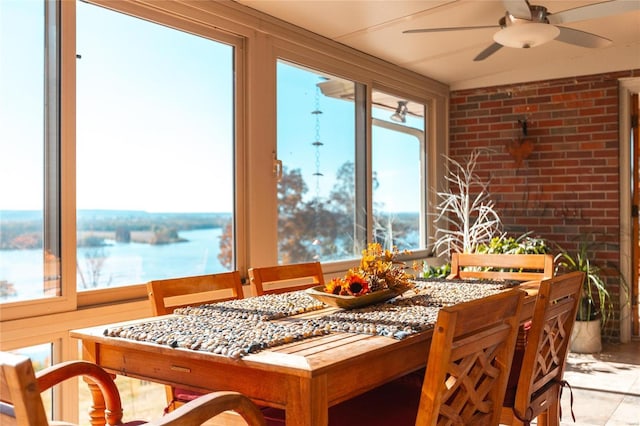 dining area featuring a water view, ceiling fan, and brick wall