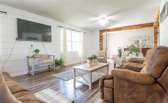 living room featuring ceiling fan, wood walls, hardwood / wood-style floors, and a textured ceiling