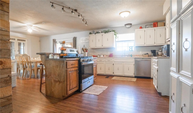 kitchen featuring a textured ceiling, white cabinets, a center island, dark wood-type flooring, and stainless steel appliances