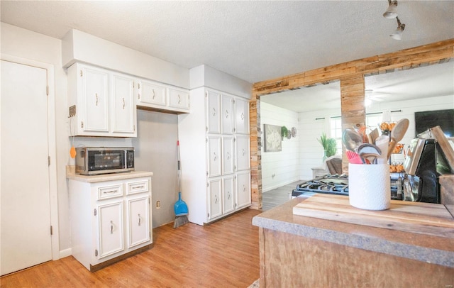 kitchen with light hardwood / wood-style floors, a textured ceiling, white cabinets, and wood walls