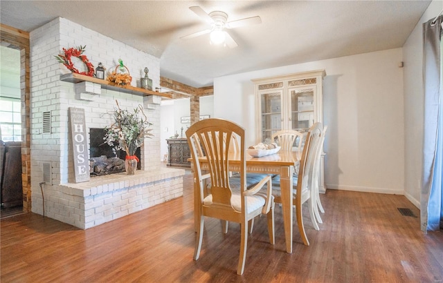 dining area with ceiling fan, wood-type flooring, and a fireplace