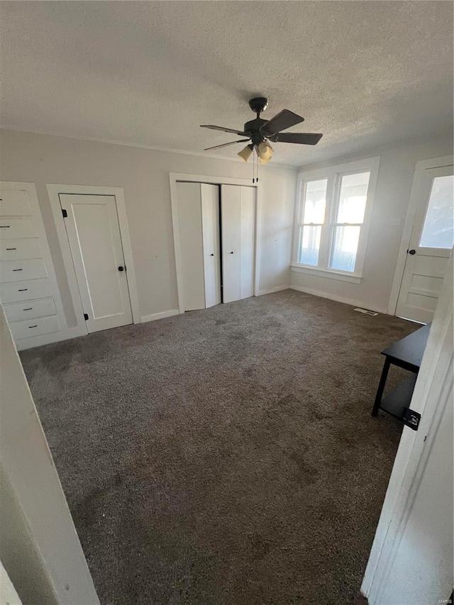 unfurnished bedroom featuring dark colored carpet, a textured ceiling, and ceiling fan