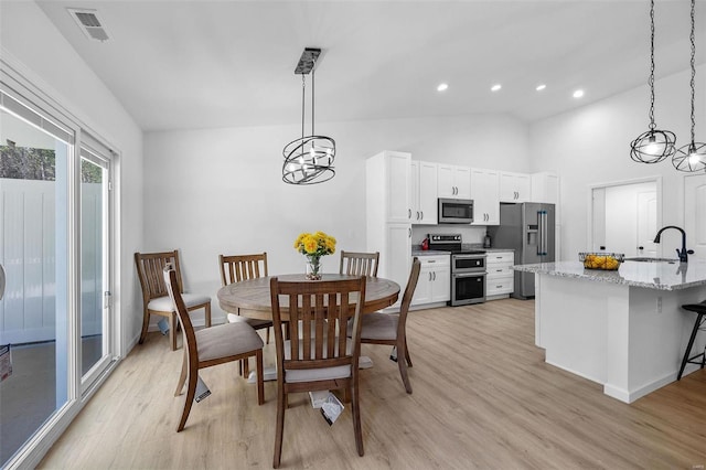 dining space featuring sink, light hardwood / wood-style flooring, and high vaulted ceiling