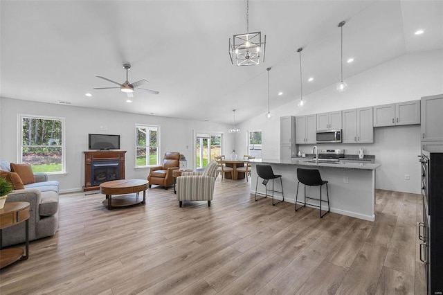 living room with ceiling fan with notable chandelier, high vaulted ceiling, sink, and light hardwood / wood-style flooring