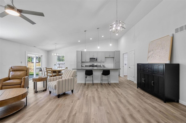 living room featuring high vaulted ceiling, ceiling fan with notable chandelier, light hardwood / wood-style floors, and sink