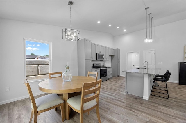 dining space with sink, a notable chandelier, light hardwood / wood-style floors, and high vaulted ceiling