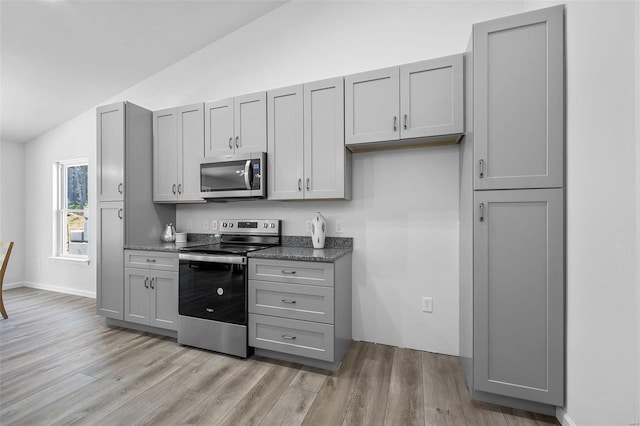 kitchen with stainless steel appliances, lofted ceiling, gray cabinetry, and light hardwood / wood-style floors