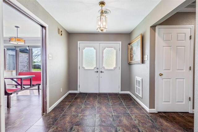 foyer with dark tile patterned floors, french doors, and a chandelier