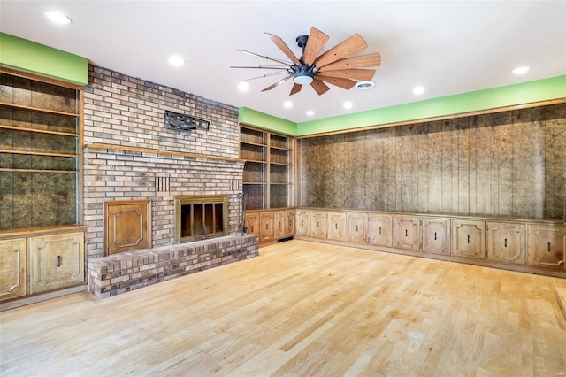 unfurnished living room with built in shelves, a brick fireplace, ceiling fan, and light wood-type flooring