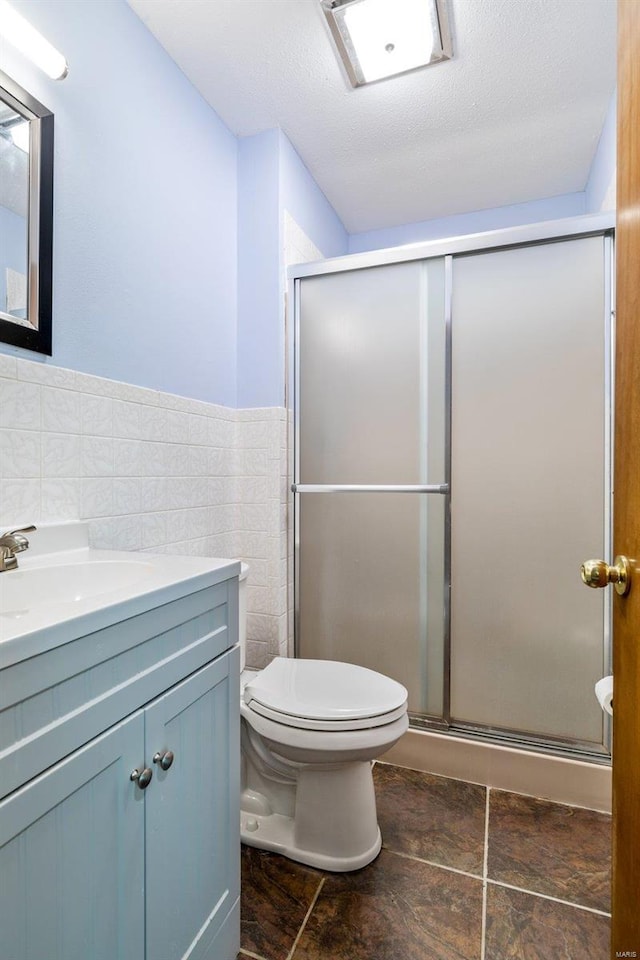 bathroom with toilet, an enclosed shower, tile walls, a textured ceiling, and vanity