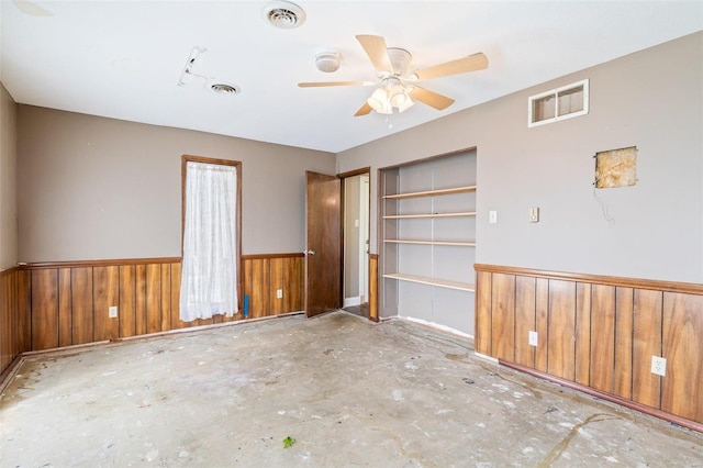 spare room featuring concrete flooring, wooden walls, and ceiling fan