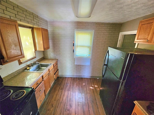 kitchen with dark wood-type flooring, freestanding refrigerator, a sink, and brick wall