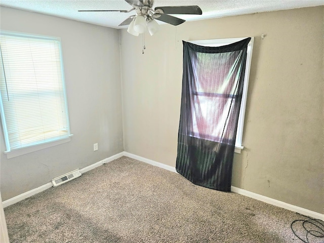 empty room featuring a textured ceiling, carpet flooring, visible vents, and a healthy amount of sunlight