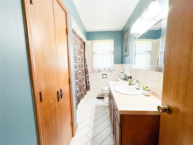 bathroom featuring tile patterned flooring, vanity, toilet, and tile walls