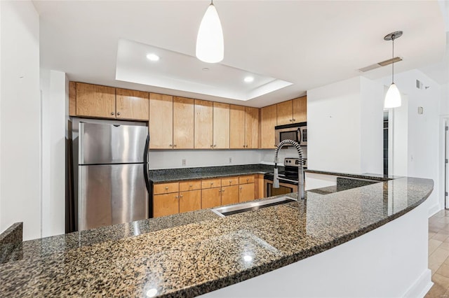 kitchen with pendant lighting, a raised ceiling, sink, dark stone countertops, and appliances with stainless steel finishes