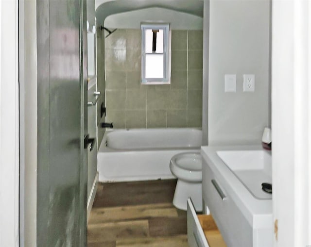 full bathroom featuring hardwood / wood-style floors, tiled shower / bath combo, vanity, and toilet