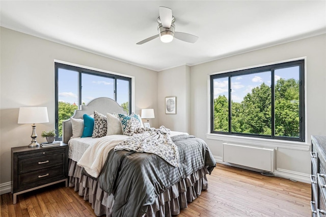 bedroom featuring multiple windows, ceiling fan, radiator heating unit, and light wood-type flooring