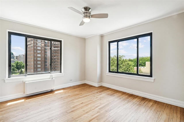 spare room featuring ceiling fan, ornamental molding, radiator, and light wood-type flooring