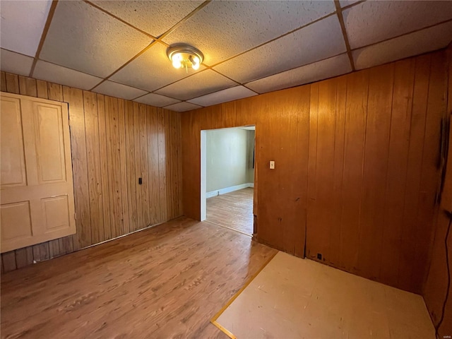 unfurnished room featuring a paneled ceiling, wooden walls, and wood-type flooring